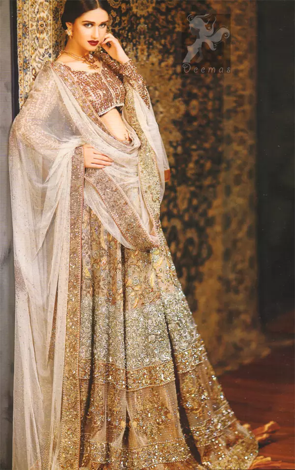 Ivory white and fawn bridal dress for the Walima function.Fully embroidered full-sleeved blouse. Lehenga features stunning embellishments. An embellished border is implemented on four sides of the dupatta. Crystal stones are crafted all over the dupatta. Ivory White Fawn Bridal Blouse And Lehenga.