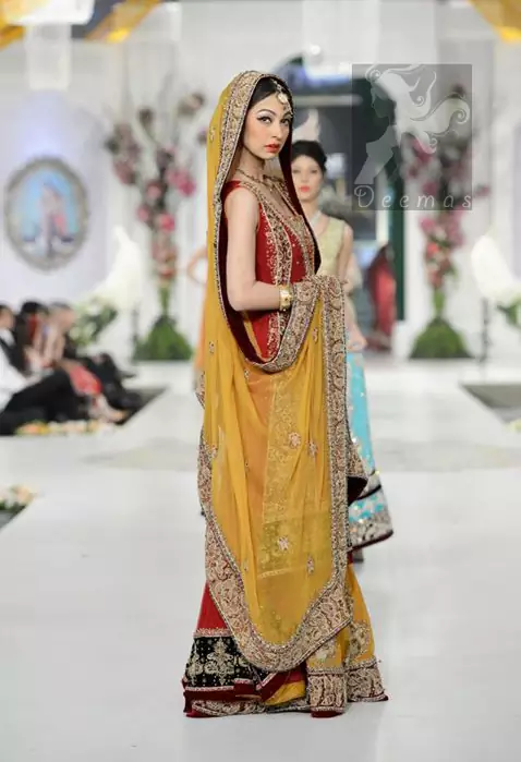 The deep red chiffon is front open, and the back train gown has an orange lehenga and an embroidered dupatta. The gown has been adorned with an embellished neckline. A work border has been implemented on the centre slit of the gown.