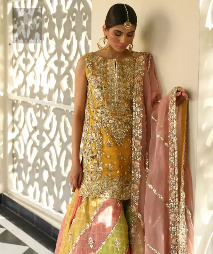 Amber shirt adorned with mainly light golden embellishment on neckline, hemline and side slits. Pink peach dupatta adorned with embellished border and stripes. Multiple color sharara adorned with border on hemline, stripes and motifs.