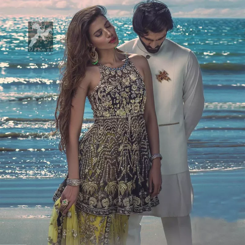 Charade net peplum having halter neckline. Peplum adorned with light golden, pearls and mix embellishment. Husk net sharara and dupatta. Sharara having hemline and small motifs spray all over it. Dupatta having zigzag border on sides, beautiful shapes of motifs on small sides (pallu) and appliqued with charade.