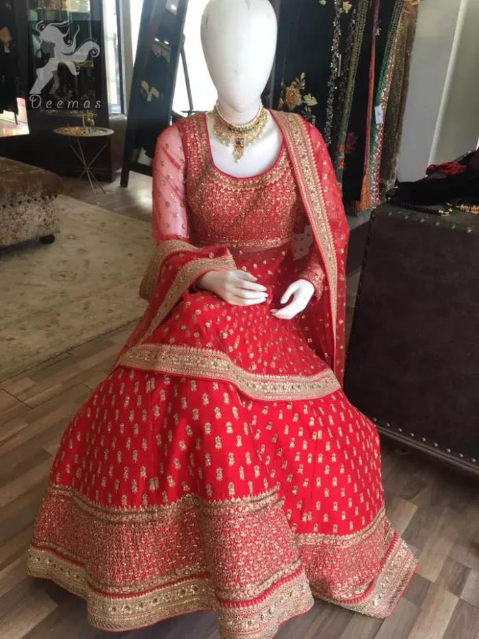 Simple but elegant deep red bridal blouse having dull golden and light antique embellishment. Appliqued with bright red fabric. Red lehengha having large borders of hand embellishment and small motifs spray above the hemline. Same border as on lehengha has been implemented on dupatta with motifs spray all over it.