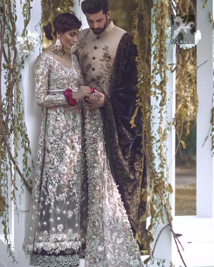 Light grayish fawn net maxi and dupatta. Bridal maxi adorned with silver, light golden, antique shades and colorful thread embellishment. Light grayish fawn net dupatta adorned with embellished border and large motifs all over it. Blackcurrant velvet sharara adorned with silver and light golden embellished border.