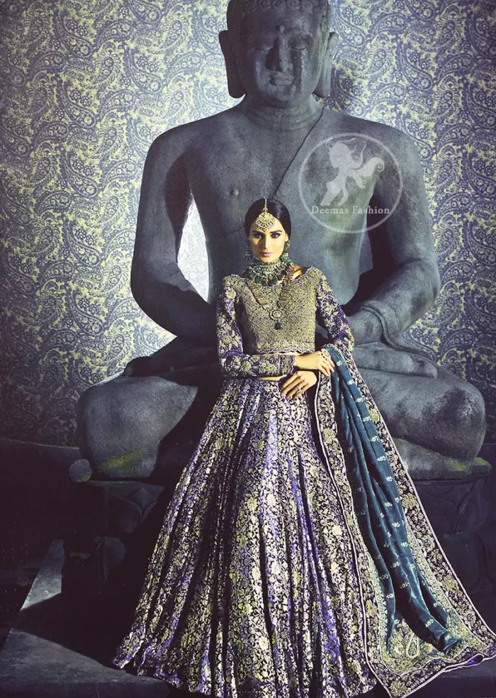 Violet Blue Blouse is of velvet fabric. It is heavy embellished full sleeves blouse featuring antique and golden shaded kora, dabka, resham, naqshi, pearls, crystals and swarovski. Blouse is fully scalloped with blue bayoux resham outline. Sleeves are adorned with floral work and sprinkling sequins/naqshi on it, while bodice having criss cross pattern all over it. It comes with raw silk lehengha which is adorned with block printing and the touch of hand embellishment. It is artistically coordinated with blue bayoux dupatta which is adorned with fully embellished appliqued borders. Borders are accompanied by delicate work along its internal sides. There are four embellished heavy flowers on corners and small floral pattern all over it.