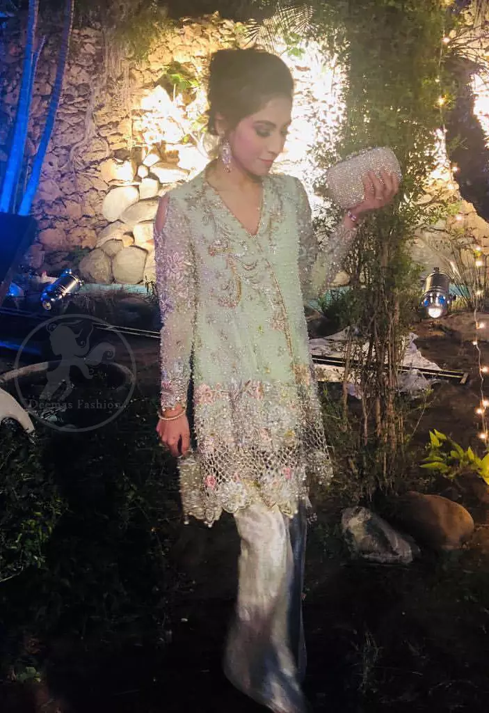 This short frok is decorated with thread, kora, dabka, tilla, sequins and swarovsky. It is embellished with floral thread embroidery. Sleeves are fully embroidered and adorned with cold shoulder design. It is decorated with intricate cutwork on hemline. It is further enhanced with embroidered scalloped border on hemline which adds to the look. It comes with brocade bell shaped pants. It is beautifully coordinated with chiffon dupatta which is sprinkled with sequins all over it.
