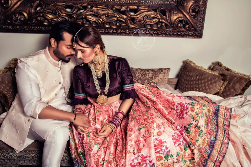 This outfit is a timeless beauty. Dark purple self-printed blouse is decorated with applique. The raw silk classic lehenga is adorned with digital print. Its floral print is further decorated with swarovski, tilla, kora dabka . Its beautiful printed border adds to the look. This outfit is beautifully coordinated with peach pink dupatta with heavy embroidered borders.