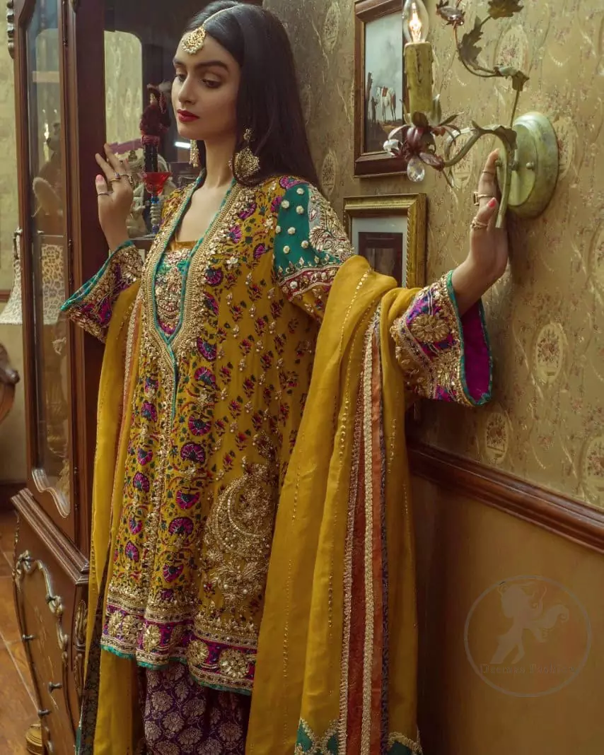 This outstanding angrakha shirt embellished with floral thread embroidery. It is allured with resham, kora dabka, tilla and pearls. Sleeves are decorated with gotta lace and floral embroidery. Embroidered applique on hemline adds to the look. It is beautifully paired up with magenta sharara with gotta criss cross patterns. It comes with chiffon goldenrod dupatta embellished with pea green applique.