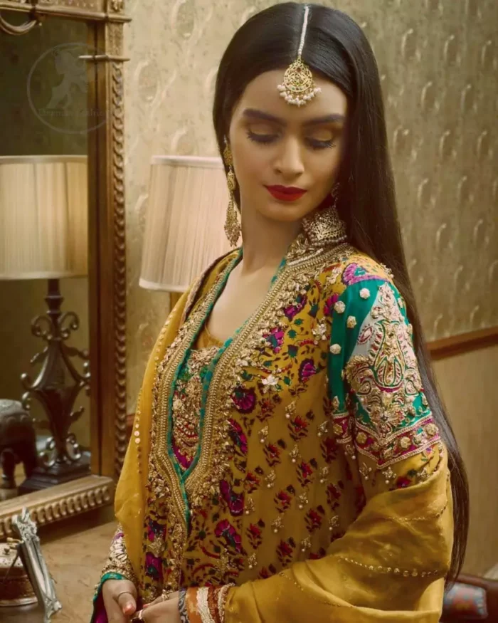 This outstanding angrakha shirt embellished with floral thread embroidery. It is allured with resham, kora dabka, tilla and pearls. Sleeves are decorated with gotta lace and floral embroidery. Embroidered applique on hemline adds to the look. It is beautifully paired up with magenta sharara with gotta criss cross patterns. It comes with chiffon goldenrod dupatta embellished with pea green applique.