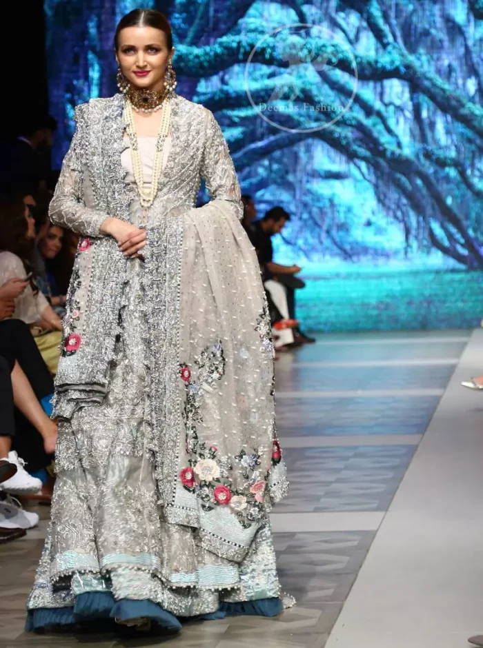 This outfit is a timeless beauty. It is heavily embellished with silver gold kora dabka, Sequins and swarovski crystals. This exquisite Pishwas is fully decorated with floral motifs patterns all over it. It is further enhanced with multiple colored Foral thread embroidery. The applique border of pishwas is ornamented with small silver pearls. It comes with embellished lehenga which has small sized sprinkled floral motifs all over. This Outfit is beautifully coordinated with matching Dupatta with heavy embroidered borders.