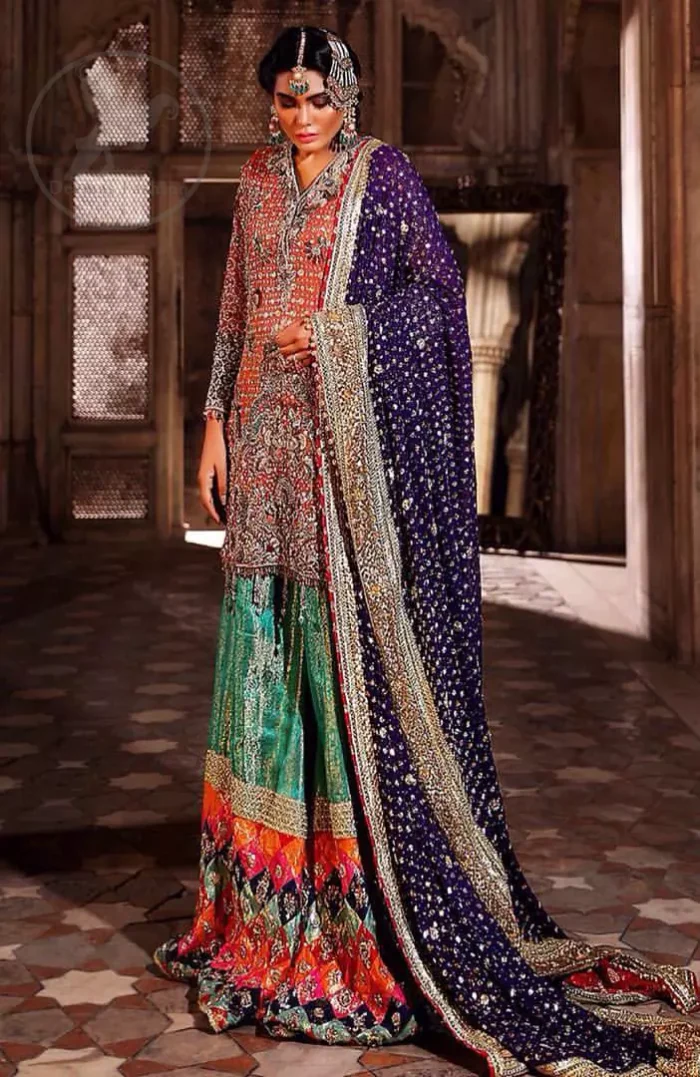 This unique bridal dress is beautifully sculptured with floral thread embroidery. It is meticulously highlighted with silver and antique kora dabka, tilla, sequins and pearls. It is artistically paired up with brocade gharara which is embellished with different color applique. It comes with chiffon dupatta which has four sided embellished border and sprinkled with sequins all over it.