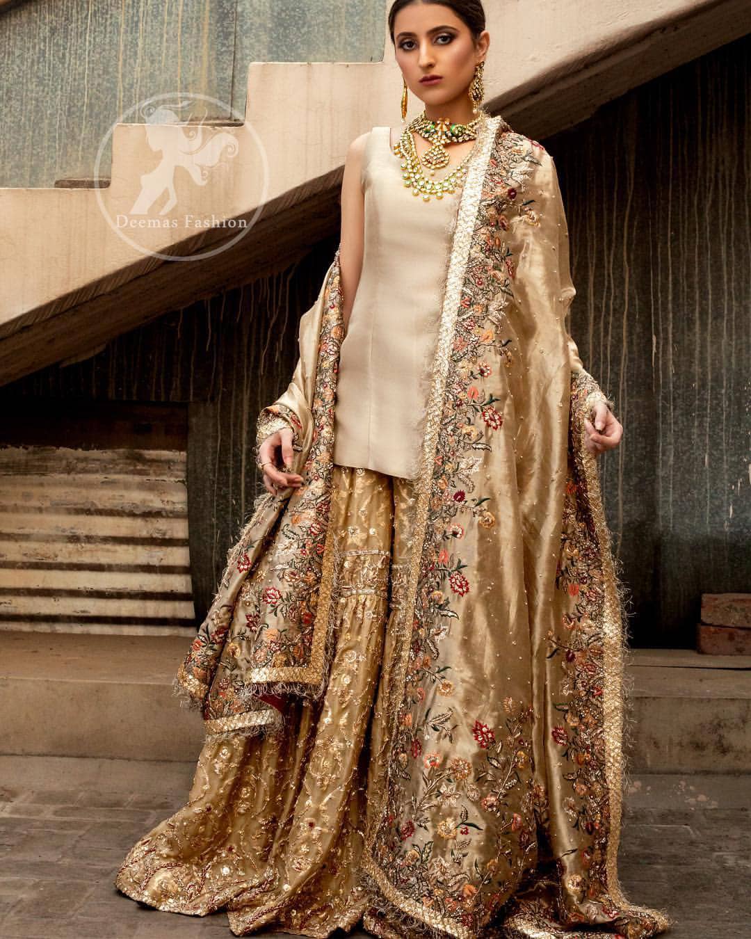 Ivory plain shirt is paired up with golden traditional gharara done with floral motifs all over. It is beautifully matched with golden dupatta with colorful embellished motifs at both lengths and lace border finished around dupatta.