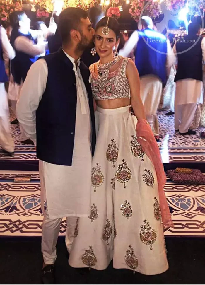 The blouse is beautifully embellished with cutwork embroidery enhanced with silver gold kora dabka, kundan and sequins work. It is paired up with ivory lehenga with colorful pattern embellishment ornamented with kora dabka, and colorful thread embroidery. It comprises with peach dupatta sprinkled sequins all over.