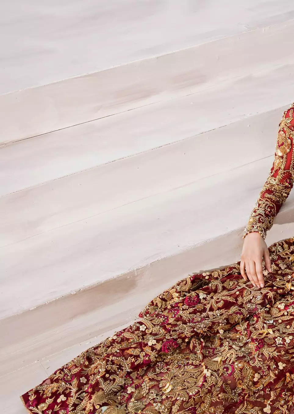 The grand maroon bridal stands out due to its uniqueness and the perfect fusion of modern cut and traditional embroidery. This halter neckline maxi is done with heavy embellishment of golden kora dabka, kundan, tilla, pearls and sequins work. It is further ornamented with detailed floral motifs. It is coordinated with brocade churidar pajama.