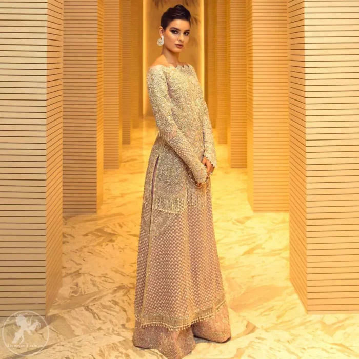 Boost your confidence and style in this glamorous attire accentuated with finest thread and zardosi work embroidery. This outfit paired up with salmon pink off shoulder long shirt embellished with thread embroidery and dull golden kora, dabka, sequins and tassels. It comes with beautifull sharara enhanced with floral motifs on the bottom. It is coordinated with chiffon dupatta which is sprinkled with sequins all over it.