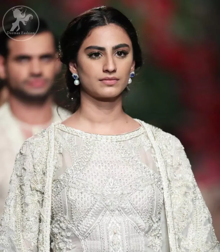Go for this trendy dress. This dress is heavily embellished with floral and geometric styled embroidery decorated with silver kora, dabka, swarovski and pearls. Gown is enhanced with scalloped border decorated with thread clusters finishing. Third quarter sleeves are embellished with floral motifs all over along with tassels at the end. Trousers is magnificently decorated with cutwork. It is coordinated with tissue dupatta which is sprinkled with sequins all over it.