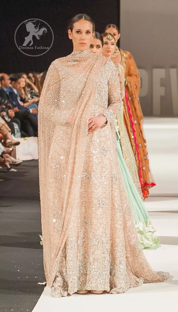 This dress is beautifully decorated with heavy embroidery. It is highlighted with dull golden kora, dabka, tilla, sequins and pearls. Fish lehengha is fully embellished.Blouse is scalloped. It comes with beautifull upper gown, sprinkled with sequins all over it. It is coordinated with chiffon dupatta which is sprinkled with sequins all over it.