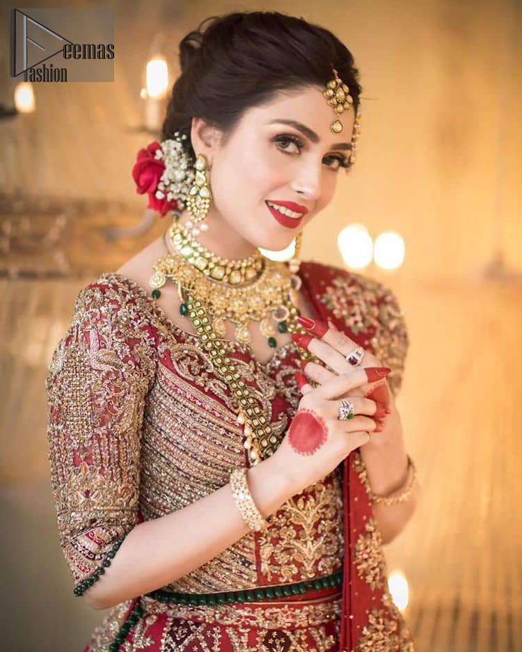 A bed of red roses translated onto a dress decorated, elaborate and flamboyant elegance. This bridal wear is perfect for your big day. The bridal stands out due to its uniqueness and the perfect fusion of modern cut and traditional embroidery. The blouse is beautifully ornamented with floral embroidery and swarovski crystals lines. Finishing with green dangling beads ball at the end. Pair it up with beautiful embroidered lehenga adorned with golden kora, dabka, tilla and sequins. Furthermore it is highlighted with geometric patterns and applique details on lehenga. It is coordinated with beautiful dupatta with thick matha patti border on two sides and intricate thin border on remaining two sides.