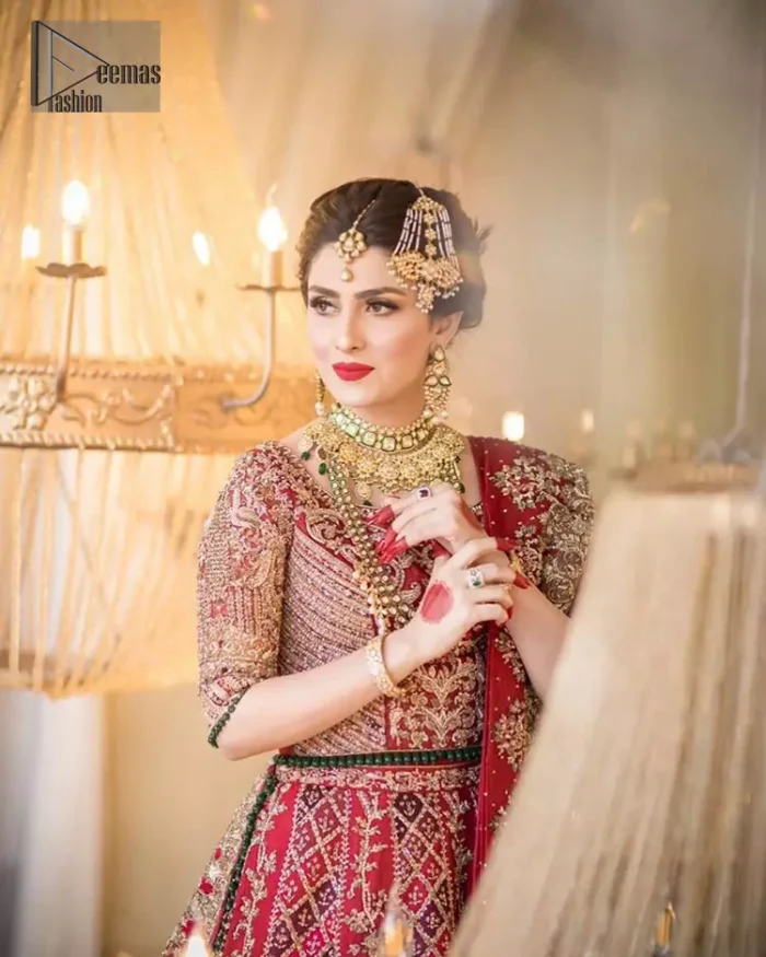 A bed of red roses translated onto a dress decorated, elaborate and flamboyant elegance. This bridal wear is perfect for your big day. The bridal stands out due to its uniqueness and the perfect fusion of modern cut and traditional embroidery. The blouse is beautifully ornamented with floral embroidery and swarovski crystals lines. Finishing with green dangling beads ball at the end. Pair it up with beautiful embroidered lehenga adorned with golden kora, dabka, tilla and sequins. Furthermore it is highlighted with geometric patterns and applique details on lehenga. It is coordinated with beautiful dupatta with thick matha patti border on two sides and intricate thin border on remaining two sides.