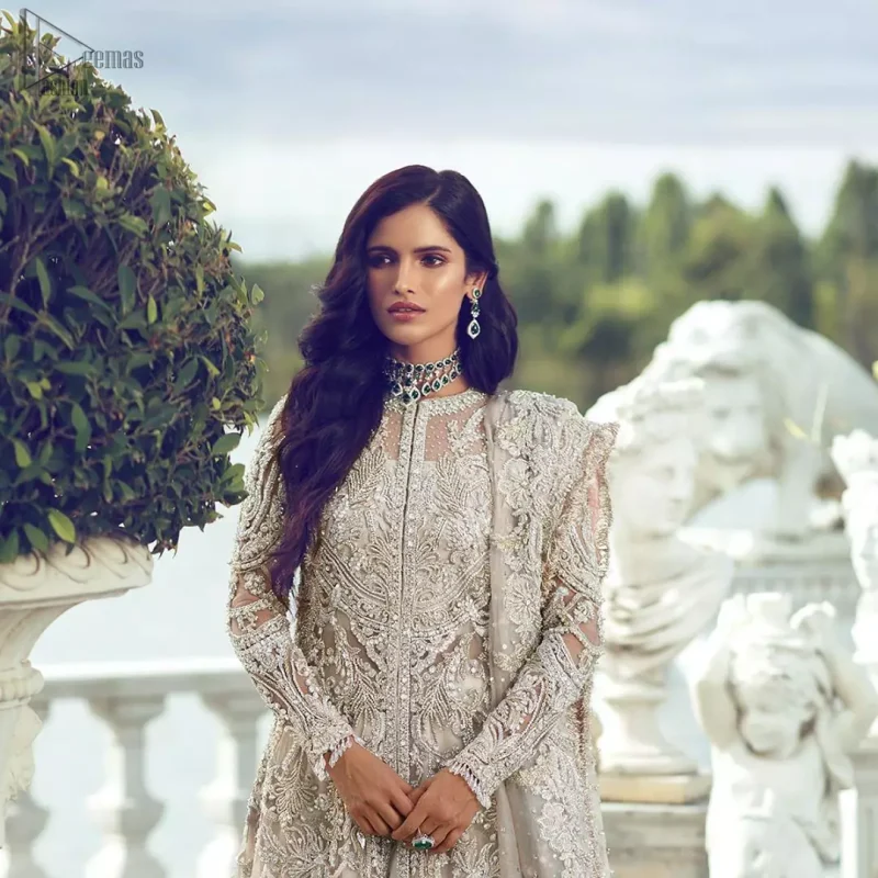 Captured in traditional silhouette, The bridal stands out due to its uniqueness and the perfect fusion of modern cut and traditional embroidery. It is highlighted with silver and light golden kora, dabka, tilla, sequins and pearls. It comes with heavily embellished front open back trail gown ornamented with floral embroidered motifs and geometric patterns. Paired up with ivory lehenga done with light gold embroidery. It is coordinated with chiffon dupatta which is sprinkled with sequins all over it. It is further furnished with four sided border.