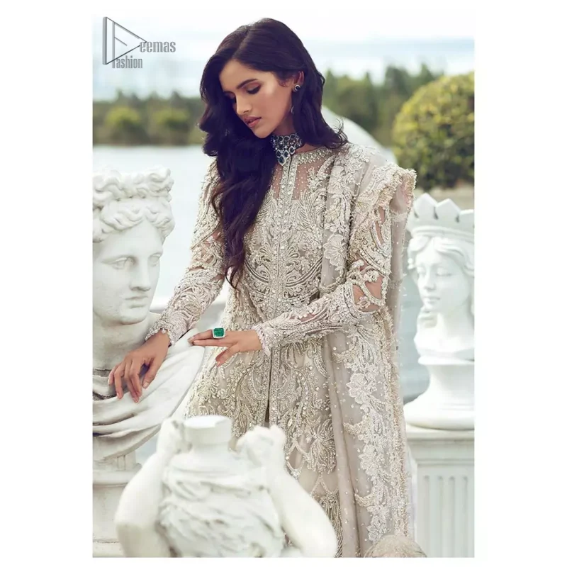 Captured in traditional silhouette, The bridal stands out due to its uniqueness and the perfect fusion of modern cut and traditional embroidery. It is highlighted with silver and light golden kora, dabka, tilla, sequins and pearls. It comes with heavily embellished front open back trail gown ornamented with floral embroidered motifs and geometric patterns. Paired up with ivory lehenga done with light gold embroidery. It is coordinated with chiffon dupatta which is sprinkled with sequins all over it. It is further furnished with four sided border.