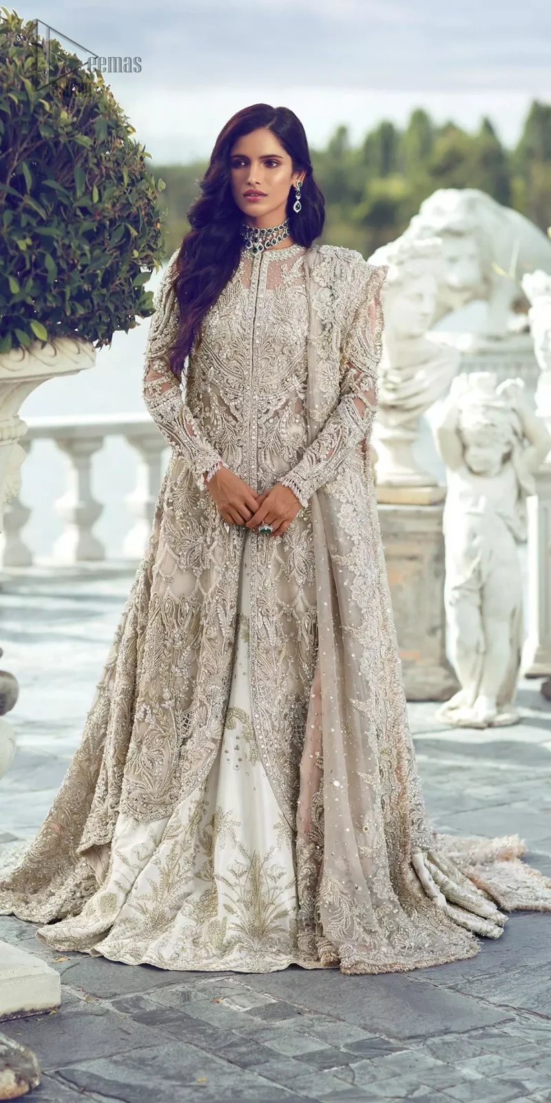Captured in traditional silhouette, The bridal stands out due to its uniqueness and the perfect fusion of modern cut and traditional embroidery. It is highlighted with silver and light golden kora, dabka, tilla, sequins and pearls. It comes with heavily embellished front open back trail gown ornamented with floral embroidered motifs and geometric patterns. Paired up with ivory lehenga done with light gold embroidery. It is coordinated with chiffon dupatta which is sprinkled with sequins all over it. It is further furnished with four sided border.