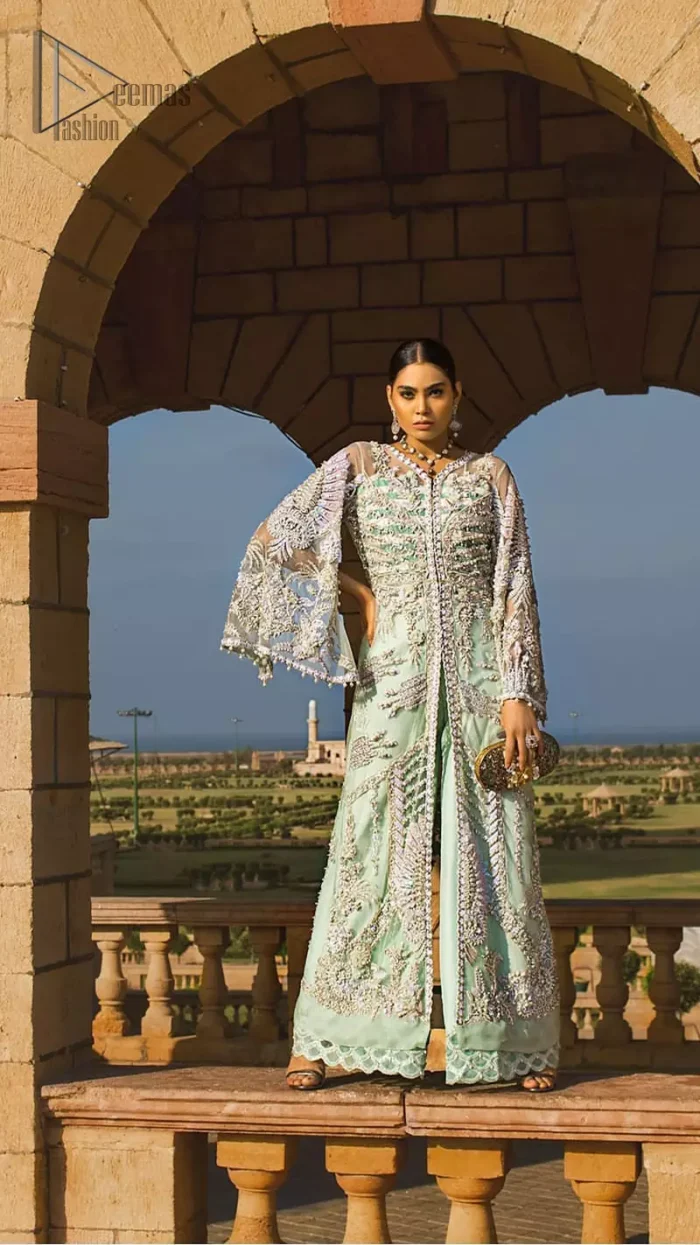Take a step towards refreshing your wardrobe with aqua front open gown and palazzo pants. This front open gown is perfected with loaded light golden and silver work. The front of the gown is heavily embellished with different styles motifs and rich embellishment on bodice. Furthermore the back of the gown and bell sleeves are also decorated with detailed embroidery and dangling balls. The palazzo pants with it is made of raw silk fabric with lace detail on the bottom. The outfit is coordinated with aqua organza dupatta sprinkled with sequins all over.