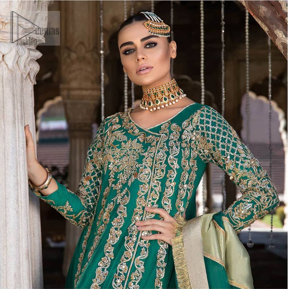 Steal the moment with our emerald green floor length angrakha emphasized with traditional neckline and intricate floral daman enhanced with light golden kora, dabka and sequins. The detailed zardosi work on sleeves and vertical panel stripes ornamented with gold kora and dabka embroidery on the bodice, the thick borders and floral bunches refined the classical royal look. Style it up with organza dupatta adorned with four sided kiran.