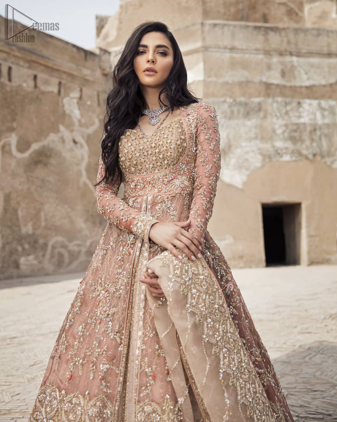 This garnet ensemble is sure to make you look like glamorous royalty with immaculate work covering every inch of the frock. The bodice of the frock is heavily embroidered with champagne zardozi work. Furthermore the hemline is ornamented with geometric patterns. It is coordinated with peach and light pink lehenga with a flowing train embellished with light golden and champagne embroidery and scattered floral motifs in a sequence.  this is an ensemble that deserves to be flaunted. Style it up with light pink dupatta having four sided embroidered border.