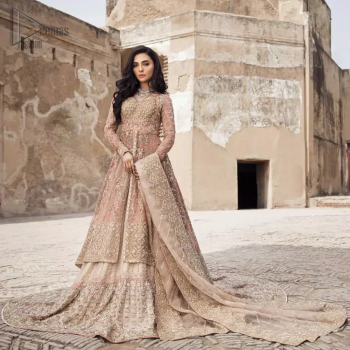 This garnet ensemble is sure to make you look like glamorous royalty with immaculate work covering every inch of the frock. The bodice of the frock is heavily embroidered with champagne zardozi work. Furthermore the hemline is ornamented with geometric patterns. It is coordinated with peach and light pink lehenga with a flowing train embellished with light golden and champagne embroidery and scattered floral motifs in a sequence.  this is an ensemble that deserves to be flaunted. Style it up with light pink dupatta having four sided embroidered border.