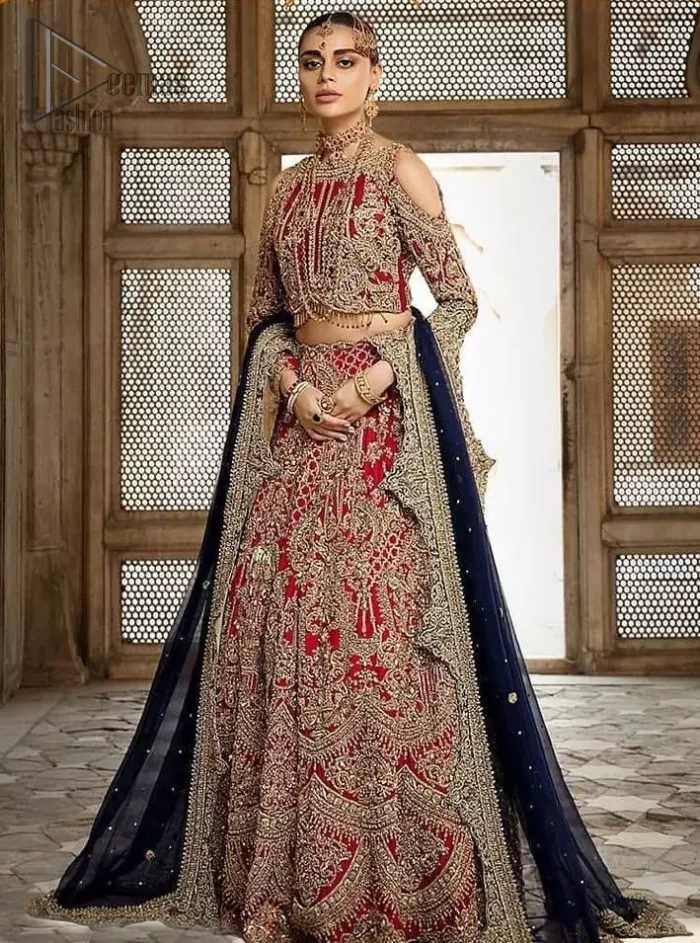 A breathtaking red traditional lehenga  paired with a detailed blouse, equally alluring make for an ensemble which is comfortably chic. The blouse is done with golden and antique shaded embroidery and finishing with tassels. Blouse having cold shoulder full sleeves. The lehenga is enhancing with the art of classical heritage showcasing the craftsmanship of kora, dabka, tilla, kundan and sequins detailed, artistically embellished to give a beautiful rhythm to the outfit. It comprises with navy blue dupatta sprinkled with sequins and four sided scalloped border. This is an ensemble that is sure to invite compliments galore.