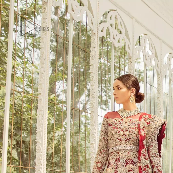 This bridal dress is perfect for your big day. Our bride makes a statement in this stunningly floraison, perfect blend of glamour and tradition with outstanding craftsmanship and gorgeous detailing. This floor length maxi is beautifully sculptured floral jhaal, floral bunches and thick scalloped hemline done with light golden kora, dabka, tilla and sequins embroidery. Exude elegance with red lehenga finessed with beautiful embellished scalloped bottom with zardosi work. The red net dupatta with chann and finishing all around the edges makes the look complete.