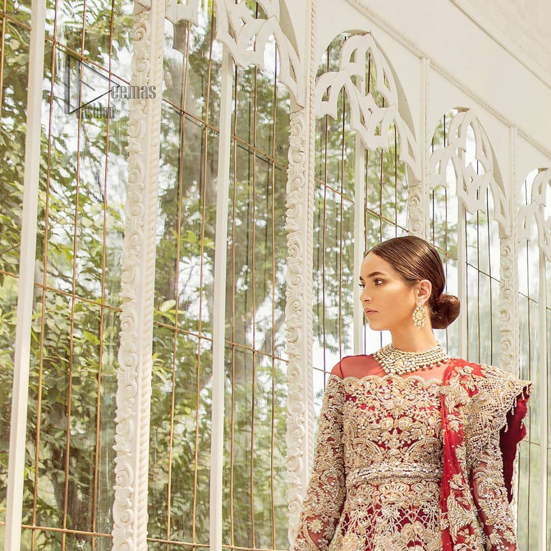 This bridal dress is perfect for your big day. Our bride makes a statement in this stunningly floraison, perfect blend of glamour and tradition with outstanding craftsmanship and gorgeous detailing. This floor length maxi is beautifully sculptured floral jhaal, floral bunches and thick scalloped hemline done with light golden kora, dabka, tilla and sequins embroidery. Exude elegance with red lehenga finessed with beautiful embellished scalloped bottom with zardosi work. The red net dupatta with chann and finishing all around the edges makes the look complete.