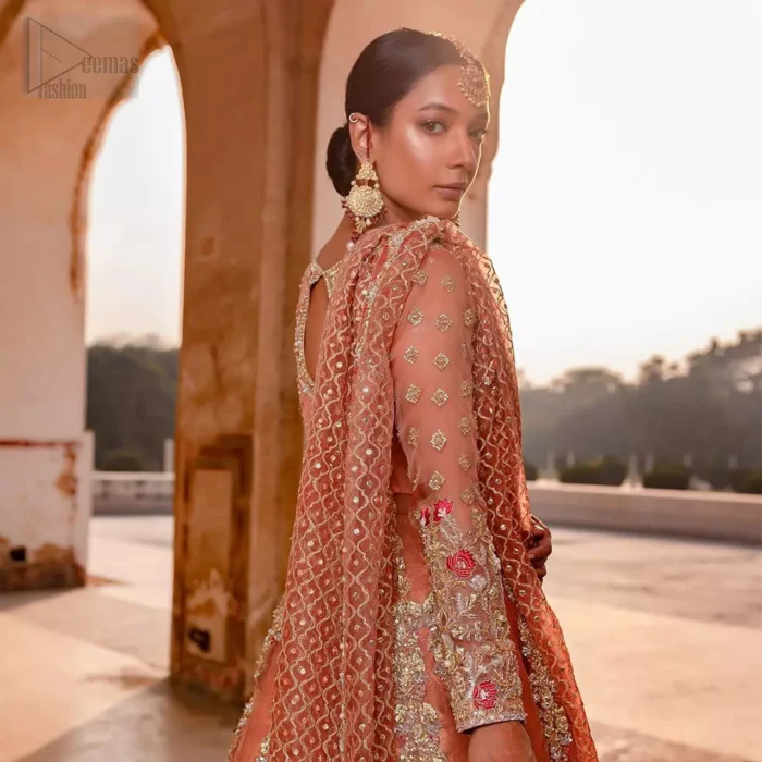 You are all set to make a lasting impact with the divine royalty of this dress. This garment is sure to make you look like glamorous with immaculate work covering every inch of the pishwas with multiple panels. This pishwas made of zardozi work with scalloped hemline and applique is everything that you need for your festivities. The brocade lehenga is beautifully adorned with thick embellished bottom with zardozi work in the shades of silver and gold. Style it up with peach organza dupatta with criss-cross patterns and floral booties on borders. This is an ensemble that deserves to be flaunted.