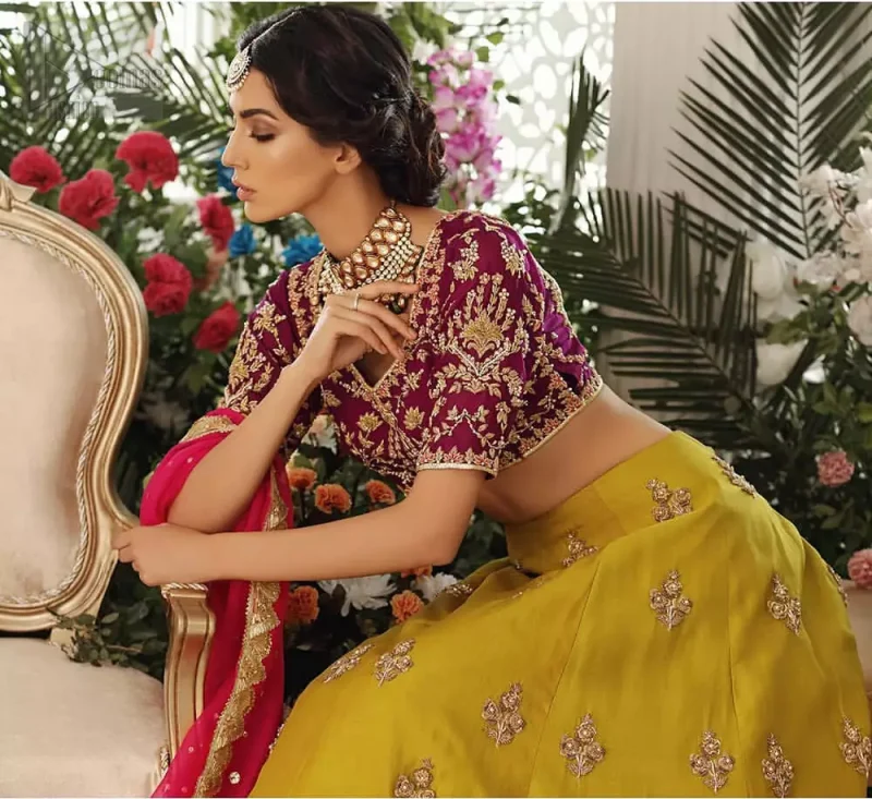 Adorn yourself with this breath-taking mehndi lehenga outfit. This beautiful mehndi dress comes with yellow lehenga with scattered beautiful embellished motifs and floral booties around a large central motif and it finished with frilled border. It is coordinated with a beautiful plum blouse adorned with zardozi work in the shades of golden and silver. Style it up with pink organza dupatta with sequins sprayed all over it along with gota finishing on all four sides.