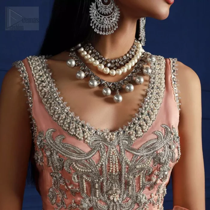 Crafted with love. This outfit is classically designed to make your memorable day beautiful as it should be. The peachy blouse is emphasized with intricate embroidery, handcrafted bootis adorned with silver embellishment finished with dangling pearls all around the edges. Compliment the look with flared lehenga which is decorated with silver kora, dabka, tilla and pearls work. Excellence of craftsmanship is evident with intricate detailing that features the use of zardozi work. The look is complete with organza dupatta finishing with frilled border.