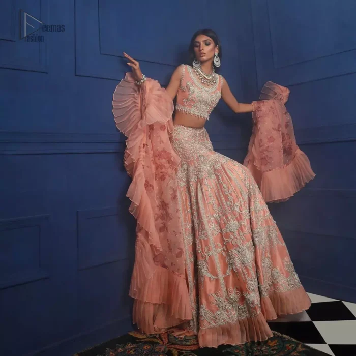 Crafted with love. This outfit is classically designed to make your memorable day beautiful as it should be. The peachy blouse is emphasized with intricate embroidery, handcrafted bootis adorned with silver embellishment finished with dangling pearls all around the edges. Compliment the look with flared lehenga which is decorated with silver kora, dabka, tilla and pearls work. Excellence of craftsmanship is evident with intricate detailing that features the use of zardozi work. The look is complete with organza dupatta finishing with frilled border.