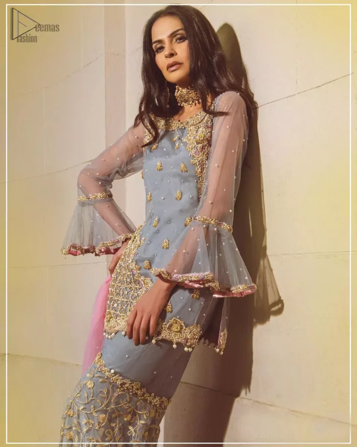 Embrace the season of festivities with this beautiful dress. The chic yet elegant outfit is decorated with golden embroidery, embellished neckline and tiny floral motifs. Borders are even more enhanced with golden zardozi detailed patterns and finished with scallops and dangling balls. Pair it up with gray sharara highlighted with floral jaal and scalloped bottom done with golden kora, dabka and tilla work. The look is complete with pink net dupatta sprinkled with sequins all over.