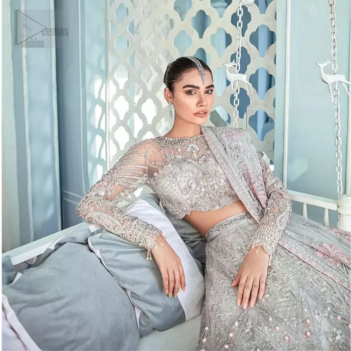 Its an unforgettable look that will effortlessly take you from day to night this festive season. Unique craftsmanship and detailed embellishments bring heavenly hued gossamer fabrics to life, creating delicate yet flamboyant pieces of art in our collection. The light gray blouse is delicately crafted with silver zardozi embellishment and finishing with scalloped sleeves and tassels. It is coordinated with lehenga which is heavily laden with sumptuous details of zardozi, applique, kora and dabka. Furthermore the lehenga is enhansed with pink applique bottom. Complete the look with light gray organza dupatta with rich embroidered floral motifs places artistically on the dupattas pallu gives a royal look.