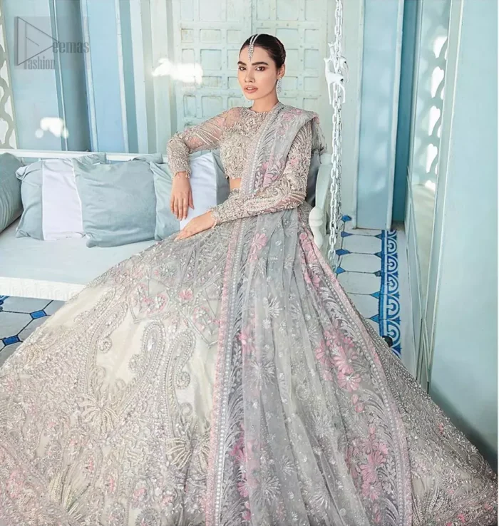 Its an unforgettable look that will effortlessly take you from day to night this festive season. Unique craftsmanship and detailed embellishments bring heavenly hued gossamer fabrics to life, creating delicate yet flamboyant pieces of art in our collection. The light gray blouse is delicately crafted with silver zardozi embellishment and finishing with scalloped sleeves and tassels. It is coordinated with lehenga which is heavily laden with sumptuous details of zardozi, applique, kora and dabka. Furthermore the lehenga is enhansed with pink applique bottom. Complete the look with light gray organza dupatta with rich embroidered floral motifs places artistically on the dupattas pallu gives a royal look.