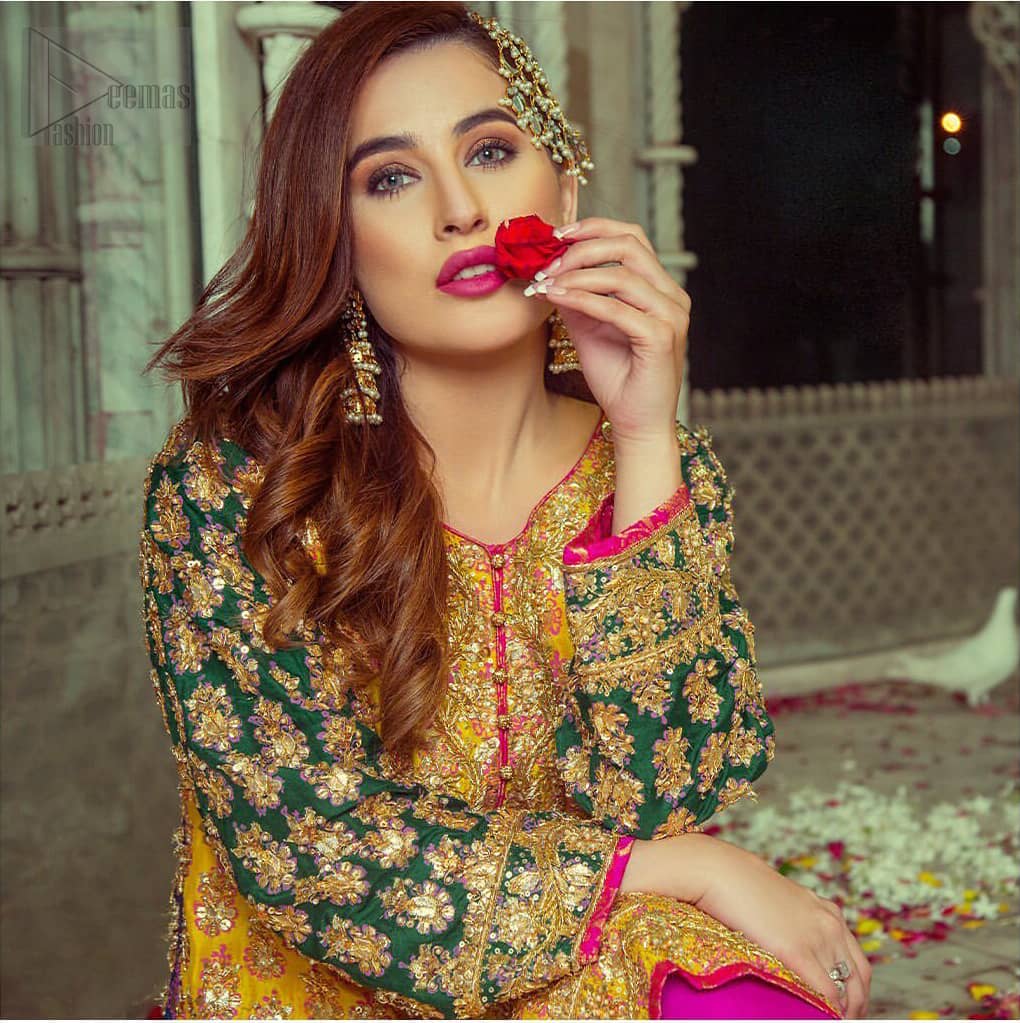Embrace the season of festivities with this beautiful dress. This beautiful mehndi dress comes with a pink capri pants with beautiful embellished applique around the bottom and the shirt is designed with vertically worked gold lines and it finished with a thick appliqued embellished border. The shirt looks more whimsical when it comes with embellished green sleeves with golden zardozi work. Balance the look with yellow organza dupatta scattered with sequins on the ground.