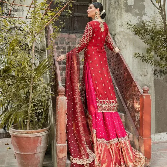 It’s ALL in the details, This breathtaking wedding dress offers comfort without compromising on style. This outfit laden with ornamental embellishments and embroidery creates such a fairytale touch to your big day. Paired with a pink sharara creates an unusual charisma wholeheartedly. Embroidery is done in the shade of golden and tiny floral motifs scattered all over the shirt. Sharara is emphasized with sequins spray and zardozi details at the bottom. Complete the look with a red dupatta having scalloped borders and scattered tiny floral motifs all over the ground.