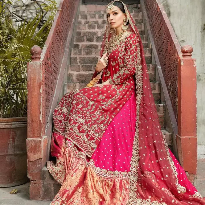 It’s ALL in the details, This breathtaking wedding dress offers comfort without compromising on style. This outfit laden with ornamental embellishments and embroidery creates such a fairytale touch to your big day. Paired with a pink sharara creates an unusual charisma wholeheartedly. Embroidery is done in the shade of golden and tiny floral motifs scattered all over the shirt. Sharara is emphasized with sequins spray and zardozi details at the bottom. Complete the look with a red dupatta having scalloped borders and scattered tiny floral motifs all over the ground.