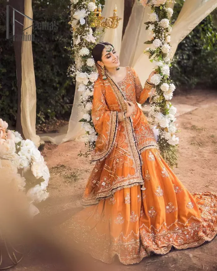 Time to treat yourself with an orange article of Deemas Fashion. This orange heartiest mealtime article will twirl your heart.  Prettify your Mehndi look with this orange short shirt that is embellished with tilla, kora and dabka work. Its rounded neckline with full sleeves gives you a genuine feeling of a bride. It is synchronized with flayer orange sharara that has an embellished border and spray of tiny floral motifs that gives a super aesthetic look to this dress. Finish this look with a net dupatta that has four sides embellished border and Kiran work.