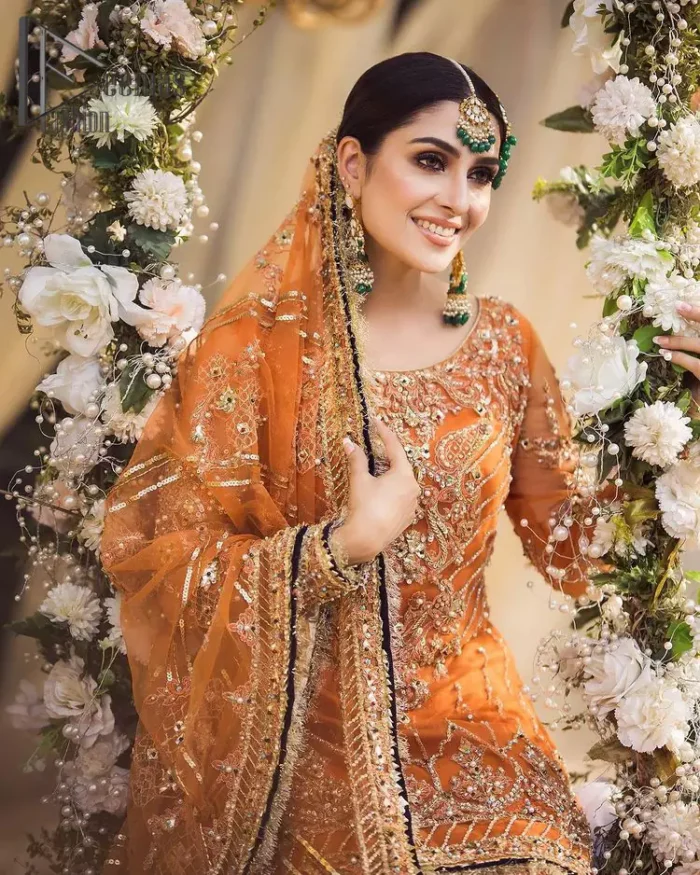 Time to treat yourself with an orange article of Deemas Fashion. This orange heartiest mealtime article will twirl your heart.  Prettify your Mehndi look with this orange short shirt that is embellished with tilla, kora and dabka work. Its rounded neckline with full sleeves gives you a genuine feeling of a bride. It is synchronized with flayer orange sharara that has an embellished border and spray of tiny floral motifs that gives a super aesthetic look to this dress. Finish this look with a net dupatta that has four sides embellished border and Kiran work.
