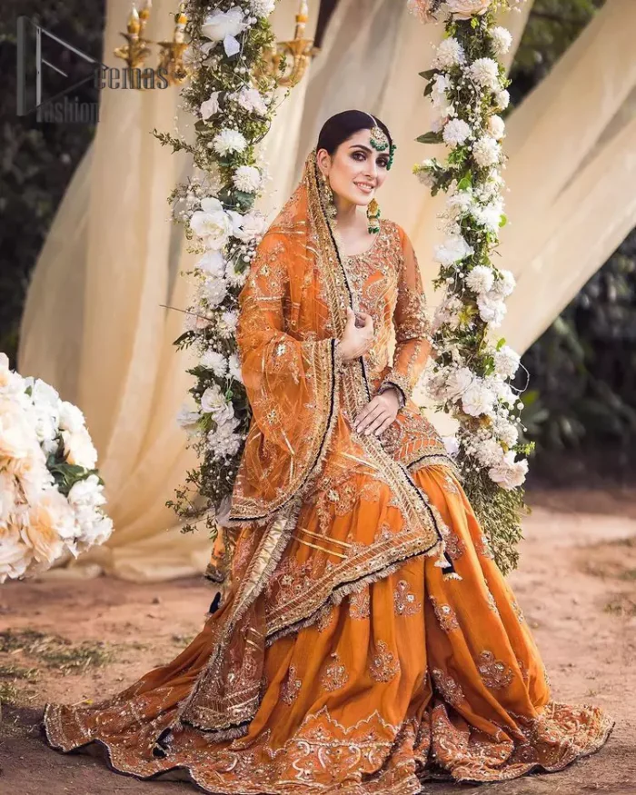 Time to treat yourself with an orange article of Deemas Fashion. This orange heartiest mealtime article will twirl your heart.  Prettify your Mehndi look with this orange short shirt that is embellished with tilla, kora and dabka work. Its rounded neckline with full sleeves gives you a genuine feeling of a bride. It is synchronized with flayer orange sharara that has an embellished border and spray of tiny floral motifs that gives a super aesthetic look to this dress. Finish this look with a net dupatta that has four sides embellished border and Kiran work.