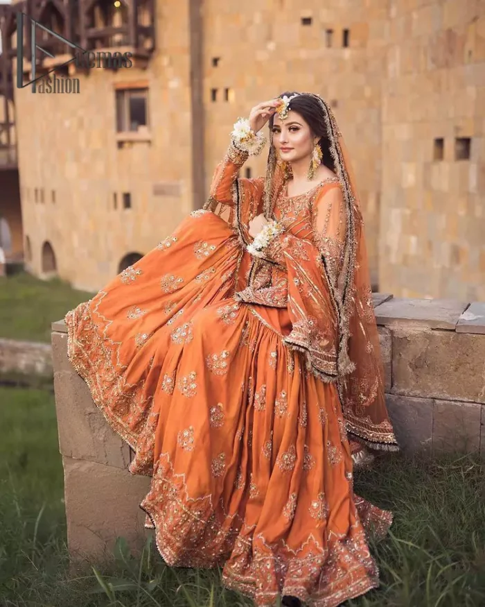 Time to treat yourself with an orange article of Deemas Fashion. This orange heartiest mealtime article will twirl your heart.  Prettify your Mehndi look with this orange short shirt that is embellished with tilla, kora and dabka work. Its rounded neckline with full sleeves gives you a genuine feeling of a bride. It is synchronized with flayer orange sharara that has an embellished border and spray of tiny floral motifs that gives a super aesthetic look to this dress. Finish this look with a net dupatta that has four sides embellished border and Kiran work.