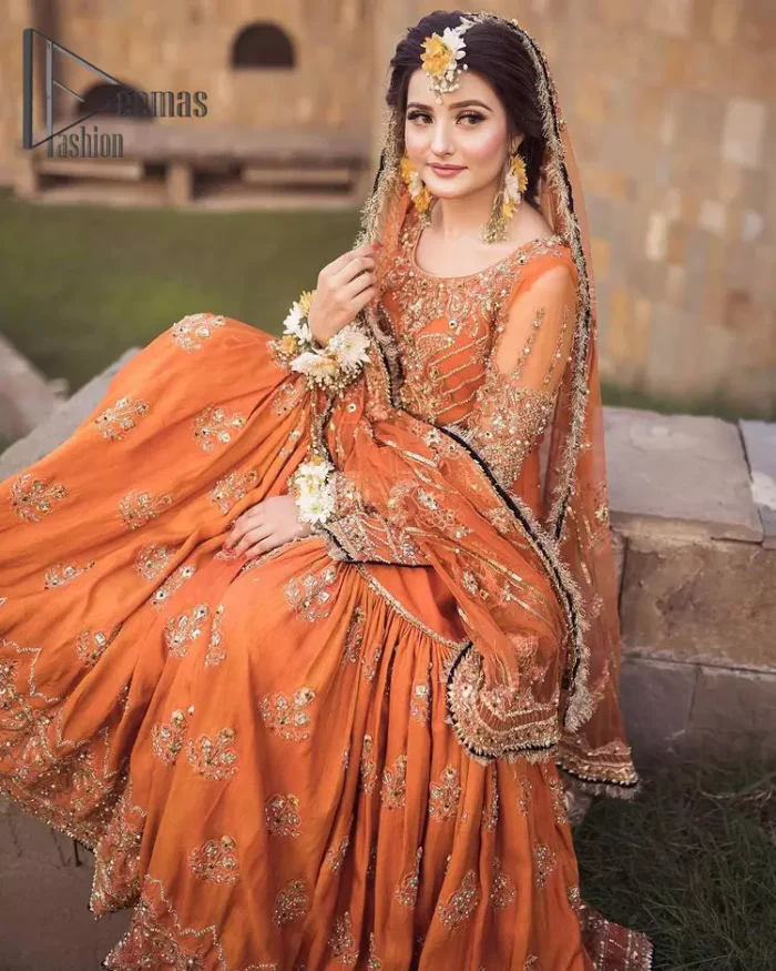 Time to treat yourself with an orange article of Deemas Fashion. This orange heartiest mealtime article will twirl your heart.  Prettify your Mehndi look with this orange short shirt that is embellished with tilla, kora and dabka work. Its rounded neckline with full sleeves gives you a genuine feeling of a bride. It is synchronized with flayer orange sharara that has an embellished border and spray of tiny floral motifs that gives a super aesthetic look to this dress. Finish this look with a net dupatta that has four sides embellished border and Kiran work.