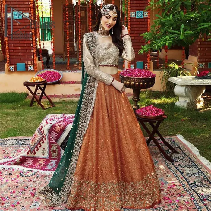 You have got plans for your mehndi? DeemasFashion got you to look!  Just go bold and bright with a beige blouse that is garnished with the same color thread embroidery and the blouse is highlighted with a square neckline and full sleeves. Further, the bottom of the blouse is adorned with red pearls that grant you a brilliant look. It is paired up with an orange lehenga that border is attractively enriched with golden embroidery and sequins spray all over. Finish this look with a green dupatta that is sprinkled with a four-sided Kiran and four sider border as well.