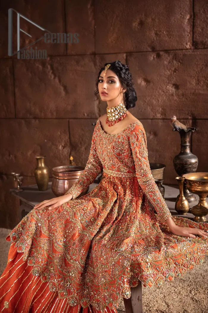 Fall in love with elements of detailing. Embrace your Mehandi style story with this orange attire serving vogue at its best. This orange frock is attractively adorned with golden embroidery that is further highlighted with kora, dabka, tilla, and antique work. And the scalloped border of the frock is just amazing so you can steal everyone's heart. In addition to this when the boat shape neckline combines with full sleeves it gives a super aesthetic scene. It is beautifully paired up with back train sharara that makes you a focus star of the day.