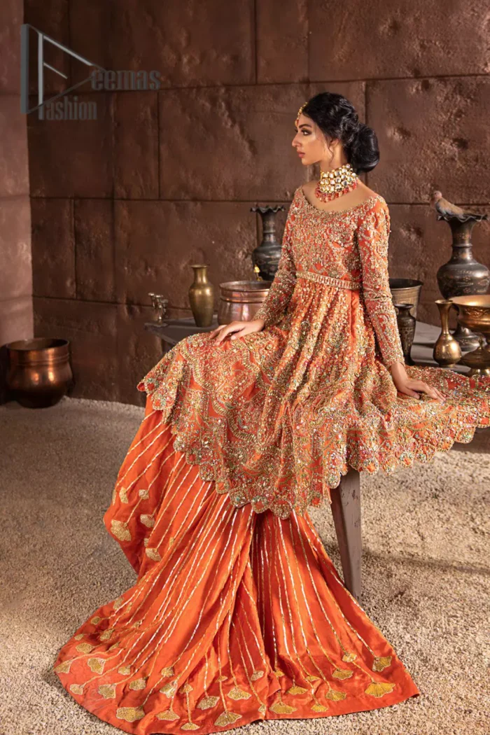 Fall in love with elements of detailing. Embrace your Mehandi style story with this orange attire serving vogue at its best. This orange frock is attractively adorned with golden embroidery that is further highlighted with kora, dabka, tilla, and antique work. And the scalloped border of the frock is just amazing so you can steal everyone's heart. In addition to this when the boat shape neckline combines with full sleeves it gives a super aesthetic scene. It is beautifully paired up with back train sharara that makes you a focus star of the day.