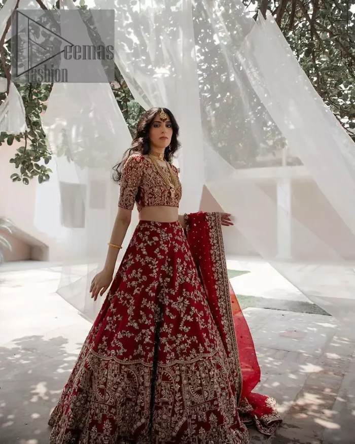 Envelop yourself into the dazzling love affair. Surprise everyone with this deep red article on your Big day. Stating this article with a deep red blouse that is handsomely styled with boat shape neckline. The half sleeves of the blouse just boost the attractiveness of the design.  In addition to this, it is delightfully furnished with golden embroidery which includes kora, dabka and tilla. Brace the blouse with a deep red fluffy lehenga that is again heavily embellished with golden embroidery that increases the beauty of the article. Complete this article with the same colour dupatta which is embellished with a four-sided borders and sequins sprayed all over just to envelop you into the dazzling love affair on your big day. 